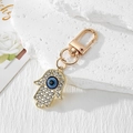 Detailopname van een gouden Hamsa Hand sleutelhanger met blauw boze oog en kristallen - Gouden Strass Hamsa Sleutelhanger