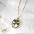 Collier élégant doré avec pendentif en résine de vrai trèfle sur un fond de pierre - Trèfle de la Chance