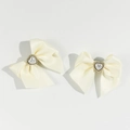 Dettaglio di fermagli a fiocco in raso crema con perle a cuore e perline dorate - Beige