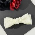 Dettaglio del fermaglio a fiocco color crema con perline su tessuto plissettato elegante - Beige