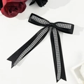 Detailed macro view of an elegant black and plaid ribbon bow hair clip with rose accents - Black