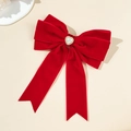 Dettaglio del fiocco in velluto rosso con cuore di perle e strass brillanti su sfondo beige - Rosso