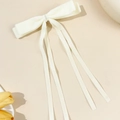 Detail of ivory velvet bow hair clip with long ribbons on a minimalist warm background - Beige