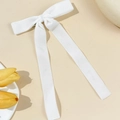 Detail view of a white velvet bow hair clip with long ribbons on a minimalist background - White