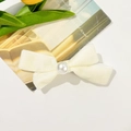 Close-up of a cream white velvet bow hair clip with a centered glossy faux pearl detail - Beige