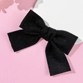 Close-up of a black velvet bow hair clip with soft texture on a pink background - Black