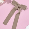 Macro shot of large taupe wool bow hair clip with elegant long ribbons on pink backdrop - Khaki