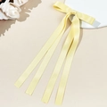 Détail d'une barrette à nœud en satin jaune pâle avec de longs rubans et texture soyeuse - Jaune