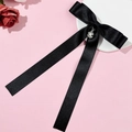 Détail d'un nœud en satin noir avec perle centrale sur un fond rose délicat - Noir