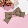 Detailed top view of dark coffee wool bow hair clip on a soft pink background - Khaki