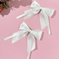 Detail van twee witte satijnen haarstrikken met lange linten op roze achtergrond - Wit