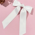 Macro shot of white satin bow hair clip with decorative wavy edges and long streamers - White