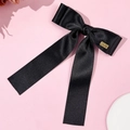 Detalle de un lazo de satén negro con un colgante Lucky dorado sobre un fondo rosa suave - Negro