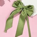 Detail shot of an olive green satin bow hair clip with long ribbons on a white tray - Green