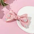 Detail of pink satin ribbon bow hair clip with pearl accents on a white display stand - Pink