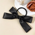 Dettaglio di un elegante elastico per capelli con fiocco in raso nero su vassoio di pietra - Nero