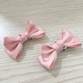 Detail of light pink satin bow hair clips showing smooth texture and metal alligator clips - Pink