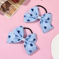 Dettaglio di elastici a fiocco azzurro con cuori blu scuro su sfondo rosa delicato - Blu
