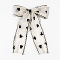 Detailed close-up of cream bow hair clip with black heart prints and wavy scalloped edges - White (Duckbill Clip - Style 2)