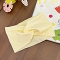 Detail view of cream twist knot baby headband on a wooden table with kids toys - Beige
