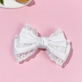 Detalle del pasador de pelo con lazo de encaje blanco y satén sobre fondo rosa suave - Blanco
