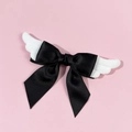 Detail of cute black satin bow hair clip with white plush angel wings on pink surface - Black