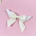 Close-up of plush angel wings and satin bow hair clip on a soft pink background - Beige