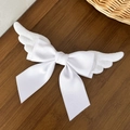 Close-up of white plush angel wings and silk bow hairpin on a dark wooden background - White
