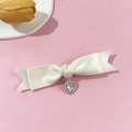 Detalle de pinza para pelo de lazo de satén crema con colgante de corazón de diamantes - Beige