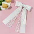 Close-up of white lace bow hair clip with floral patterns and satin ribbon streamers - White