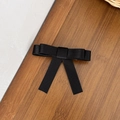 Detail of a black satin bow hair clip with long ribbons on a textured wooden background - Black