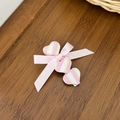 Pink ribbon bow hair clip with colorful striped heart charms on a wooden surface - Pink
