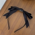 Detalle de la diadema con lazo de satén negro en capas sobre mesa de madera pura - Negro