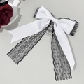 Dettaglio di un grande fiocco in raso bianco con pizzo nero e ciondolo a cuore argento - Bianco