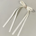 Detail showing the cream satin bow hair clip with a large pearl center and long ribbons - Beige