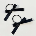 Détail de deux chouchous en satin noir avec nœuds et longs rubans sur fond neutre - Noir