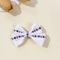Dettaglio di un fermaglio per capelli a fiocco bianco con ricamo floreale e bordi ondulati - Bianco