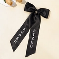 Detail of elegant black satin bow hair clip with white SUPER SIZED text on long ribbons - Black