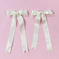 Nahaufnahme von zwei cremefarbenen Satin-Haarschleifen mit langen Schwalbenschwanzbändern - Beige