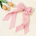 Detail of pink satin bow hair clip with long ribbons on a soft beige background - Pink