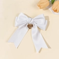 Detail of white satin bow hair clip with a gold heart-shaped charm and silk texture - White