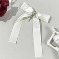 Dettaglio del fiocco in raso bianco crema con gemma a cuore e ciondolo a croce d'argento - Beige