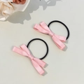 Detail von rosa Satin-Schleifen-Haargummis mit elastischen Bändern auf beigem Grund - Rosa