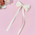 Detail van een crèmewitte satijnen haarclip met strik en lange soepele linten erop - Beige