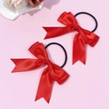 Détail de deux chouchous en satin rouge avec nœuds et longs rubans sur un fond rose doux - Rouge