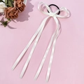 Detail eines cremeweißen Satin-Haargummis mit Schleife und langen Bändern auf Rosa - Beige