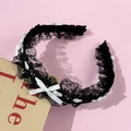 Détail d'un serre-tête en dentelle noire avec petits nœuds blancs sur fond rose - Noir