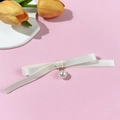 Dettaglio di un fiocco di nastro bianco con ciondolo di perla su sfondo rosa - Beige