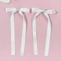 Detalle de horquillas con lazo de satén blanco y perla sobre un fondo rosa suave - Blanco
