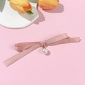 Dettaglio di spilla a fiocco in raso rosa con ciondolo di perla su sfondo elegante - Rosa